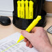 A hand holding a Universal fluorescent yellow chisel tip highlighter over a piece of paper.