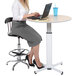 A woman sitting at a round table using a Luxor pneumatic adjustable height table with a laptop.