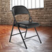 A National Public Seating black metal folding chair with a black padded seat set up in a room.