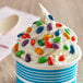 A white cup of ice cream with colorful chocolate candy toppings.