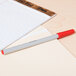 A Universal red oil-based ballpoint pen next to a notepad on a table.
