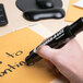 A person using an Avery Marks-A-Lot black desk style permanent marker to write on a piece of paper.