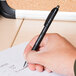 A hand using a Universal One Comfort Grip black fine point pen to write on a calendar on a table.