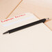 A black Universal One Comfort Grip ballpoint pen writing on a piece of paper.
