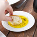 A person holding a piece of bread in a TuxTrendz bright white china oil dish full of olive oil.