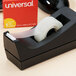 A black Universal tape dispenser on a table with a roll of clear tape in it.