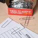 A Universal silver jumbo paper clip box on a table with paper clips inside.