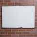 A Universal white melamine dry erase board with a marker on it mounted on a brick wall.