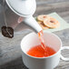 A Tuxton TuxTrendz white china teapot pouring tea into a cup.