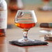 An Acopa Select brandy tasting snifter with brown liquid in it on a coaster.