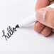 A hand writing "hello" on a piece of paper with a black Universal bullet tip dry erase marker.