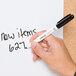 A hand using a Universal bullet tip dry erase marker to write on a white board.