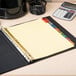 A binder with Avery 8-tab multi-color dividers and a yellow paper in it.