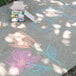 A box of Crayola 48 assorted bright colors washable sidewalk chalk on a table with chalk drawings.