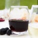 A close up of an Acopa narrow stemless wine glass filled with red wine on a table next to blackberries.