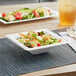 A salad in a white EcoChoice Compostable Sugarcane square bowl on a place mat.