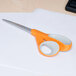 Fiskars 8" Softgrip scissors with a white and orange handle cutting a white piece of paper.