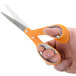 A hand using Fiskars orange and gray office scissors to cut paper.