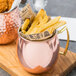 A close up of an American Metalcraft copper Moscow Mule mug filled with french fries and chicken.