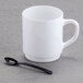 A white mug on a grey surface with a black Fineline Tiny Tasters spoon in it.