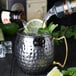 A person pouring a drink into a silver American Metalcraft hammered Moscow Mule mug with a lime.