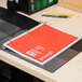 A red Universal spiral bound college ruled notebook on a table.