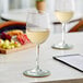 Two Acopa Select Flora wine glasses filled with white wine on a table.