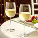 A pair of clear wine glasses filled with white wine on a table.