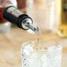 A stainless steel tapered liquor pourer with a flip cap being used to pour liquid into a glass of ice.