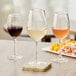 Three Acopa Select Blanc wine glasses filled with white, pink, and red wine on a table.
