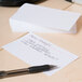 A close-up of a Universal white ruled index card on a table with a pen.