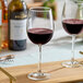 A clear 16 oz. wine glass partially filled with red wine, placed on a wooden surface.