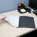 A hand holding a black and white Universal Office report cover with a clear cover and prong fasteners over a piece of paper.