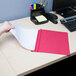 A person's hand holds a red Universal Office leatherette report cover with clear front on a piece of paper.