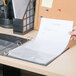 A hand inserting a piece of paper into a binder using a Universal clear non-glare sheet protector.