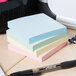 A table with a stack of Universal assorted pastel color self-stick notes and a pen.