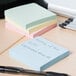 A Universal assorted pastel color self-stick note pad with writing on it next to a pen on a table.