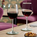 A pair of clear wine glasses partially filled with red wine, placed on coasters on a wooden table.