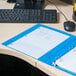 A light blue Universal Deluxe Non-Stick View Binder on a desk with papers.