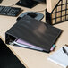 A black Universal Deluxe Non-Stick View Binder on a desk with papers and a pen.