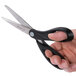 A hand holding Universal stainless steel scissors with a black handle.