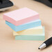 A stack of Universal assorted pastel colored self-stick notes with a pen.