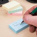 A person writing on a Universal assorted pastel color self-stick note.