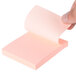 A hand holding a Universal Assorted Neon Color sticky note pad with pink paper.