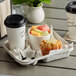 A Huhtamaki Chinet 2 cup carrier with coffee cups and a muffin on a table.