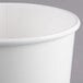 A close-up of a Huhtamaki white paper food cup with a lid on it.