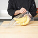 A person in a chef's uniform holding a plastic bag of bananas.