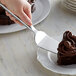 A hand using a Vollrath stainless steel pastry server to cut a piece of chocolate cake.