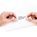 A person's hands using a white Avery mailing address label on a business card.