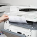 A person putting a white rectangular Avery address label into a printer.